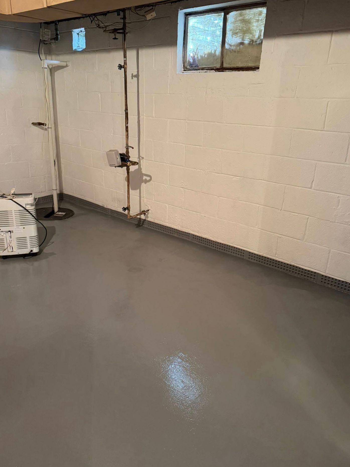 A basement with a gray floor and white brick walls.