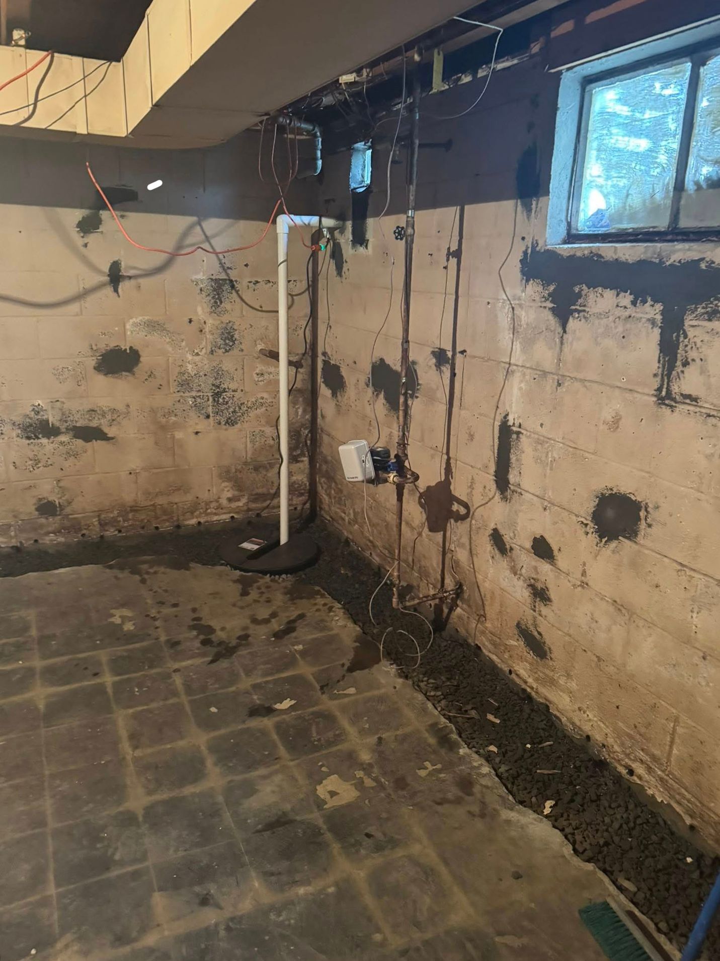 A dirty basement with a brick wall and a window.