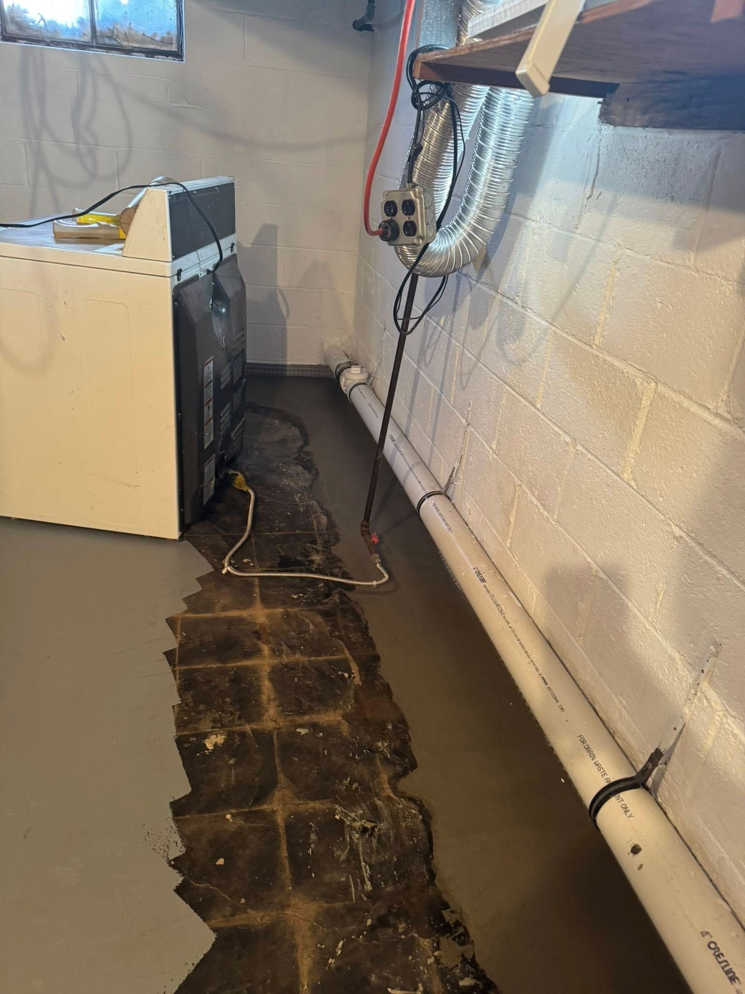 A washer and dryer are sitting in a basement next to a brick wall.