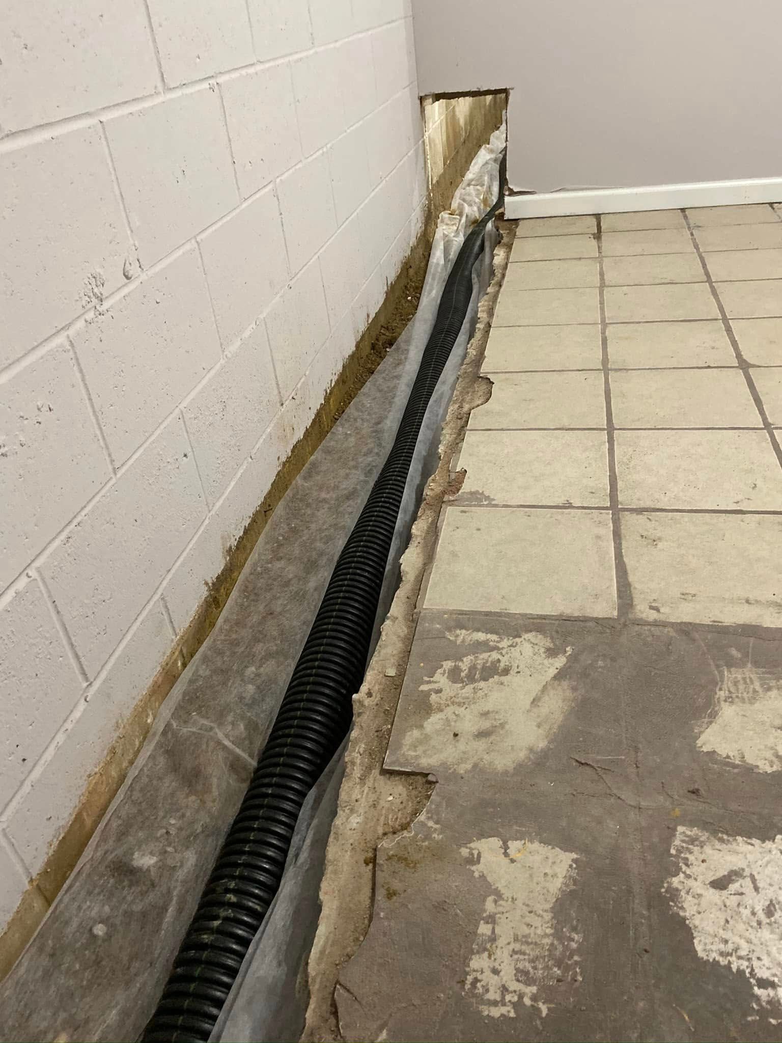 A drain pipe is being installed in a basement next to a brick wall.