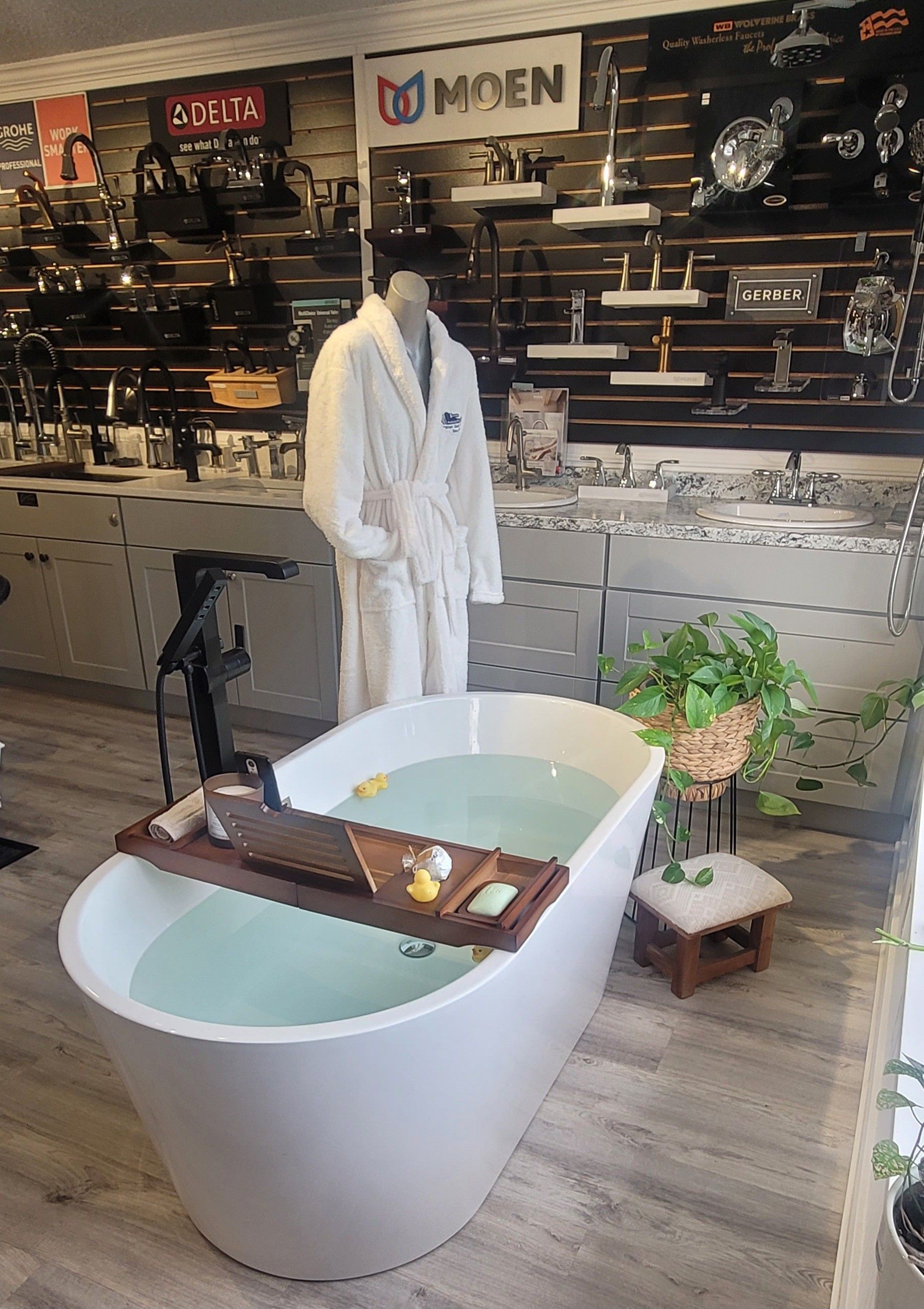 Freestanding bathtub display in a showroom, with a robe-clad mannequin and bath accessories.