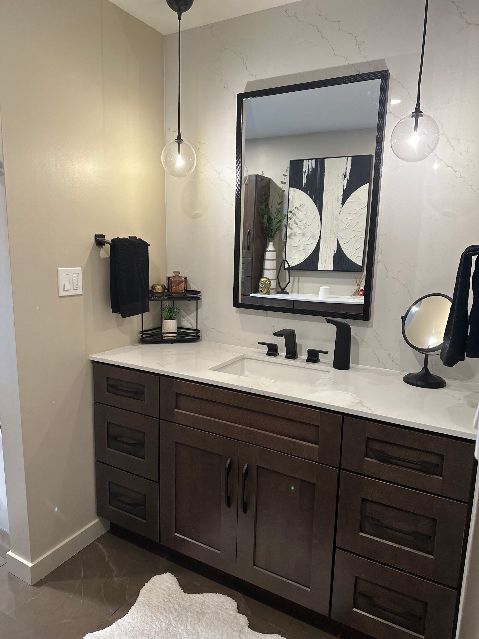 Bathroom with dark brown vanity, black framed mirror, globe pendant lights, and modern decor.