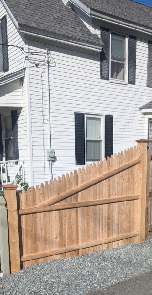 Wooden fence in front of a white house with black shutters, power lines visible.