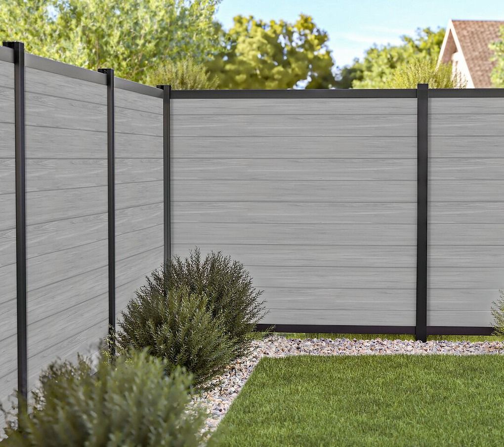 A gray fence with a black trim is in the middle of a lush green yard