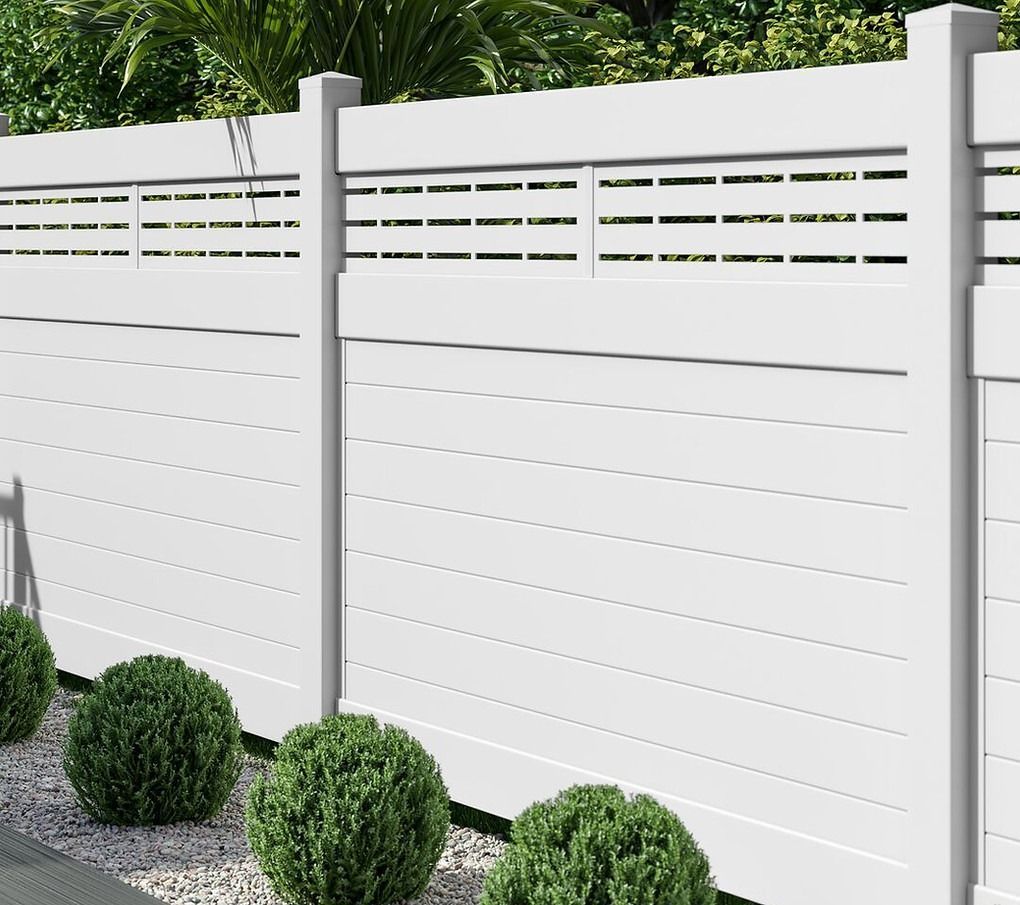 A white fence with holes in it is surrounded by green bushes