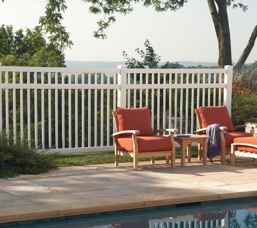 A white fence surrounds a swimming pool with chairs and tables