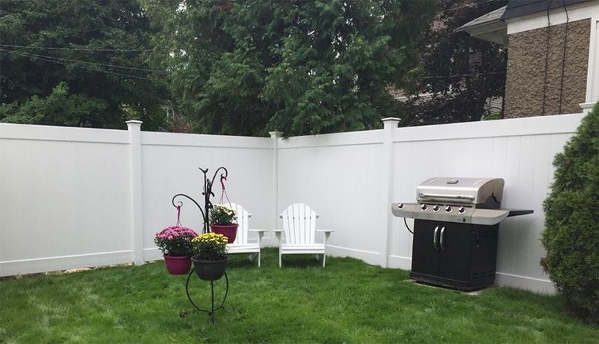 A backyard with a white fence and a grill