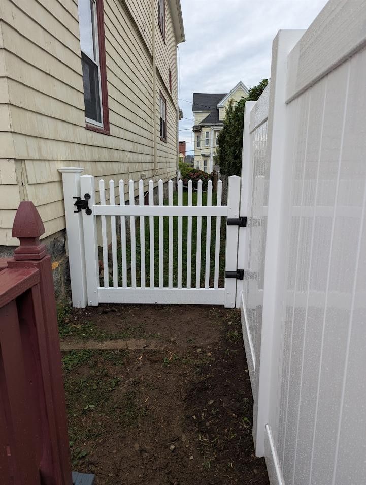 White picket gate between white fence and beige house.