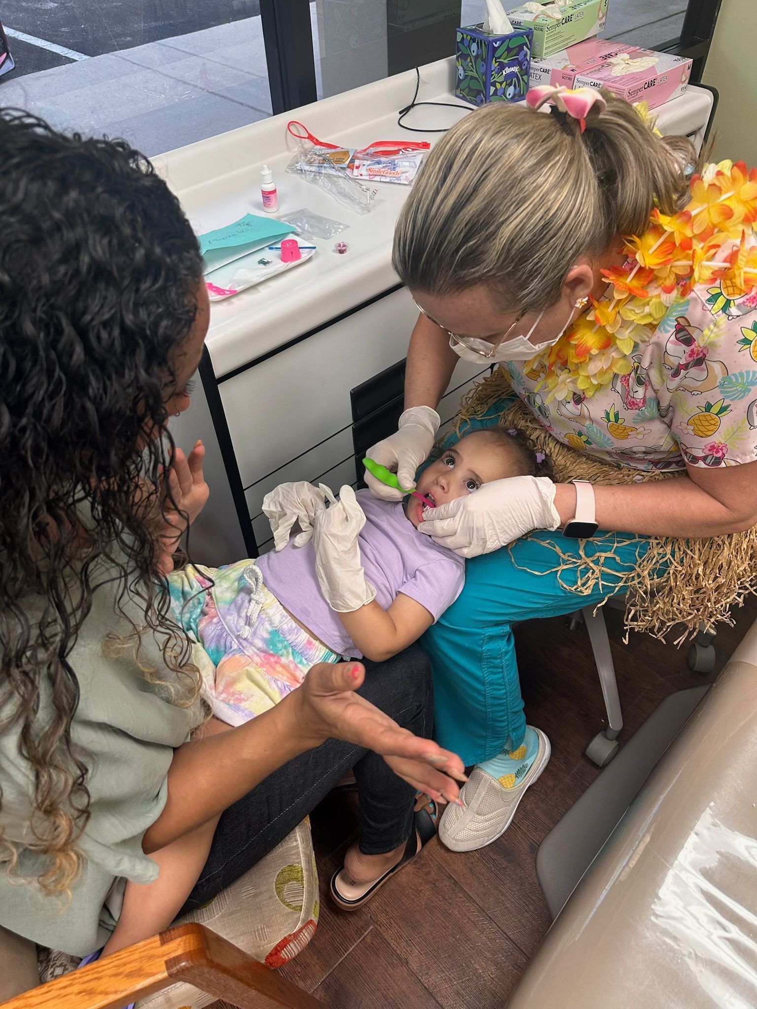 A doctor examining a baby's arm in a doctor's office. The baby sits on its mother's lap.