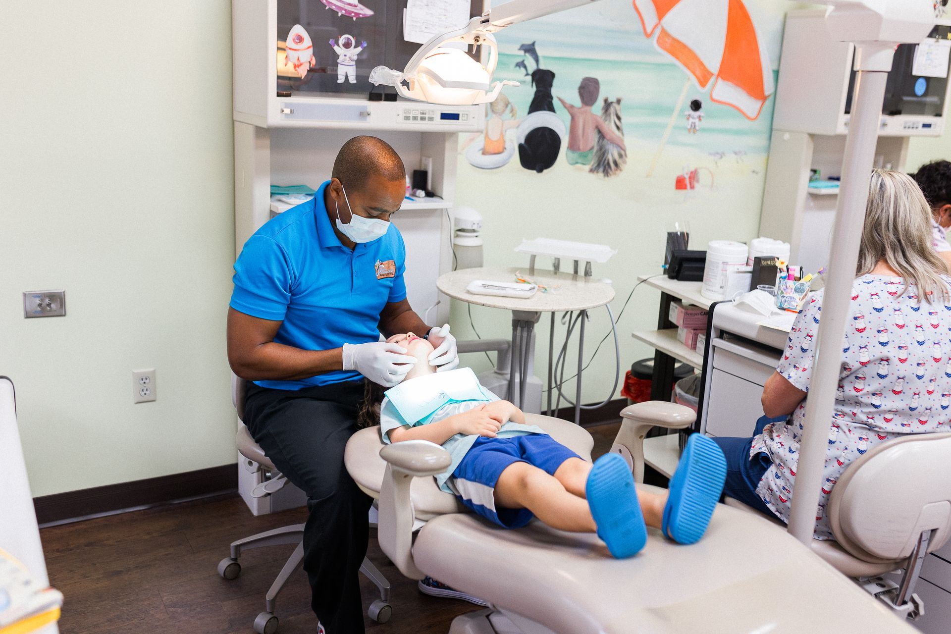 Smiling dentist with thumbs up and young girl in a dental chair, in a brightly painted dental office.