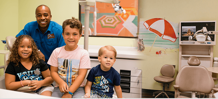 A dentist smiles with three young children in a colorful dental office. The room is decorated with beach-themed artwork.