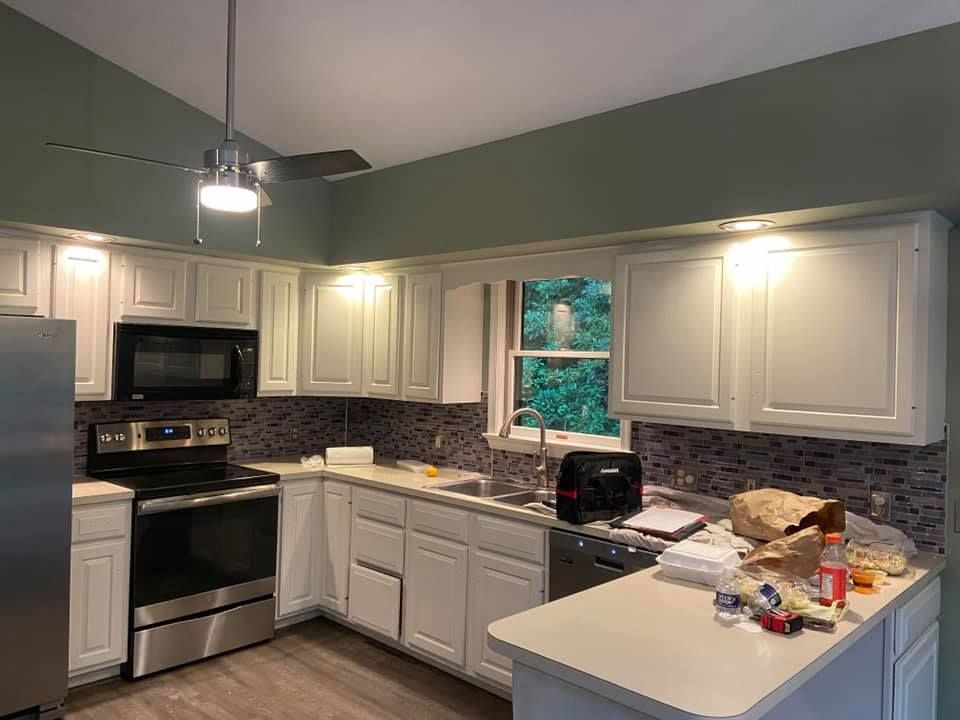 White kitchen cabinets with appliances and a dark backsplash, green wall.