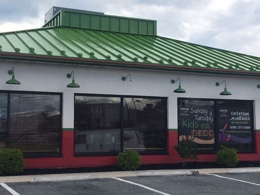 Restaurant exterior with green roof and awning. White walls, red trim, and large windows.