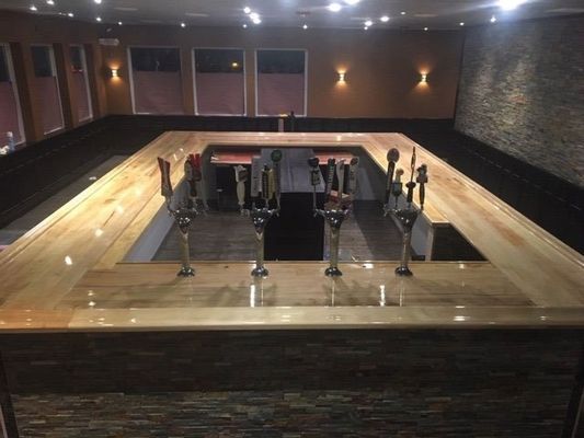 Empty bar with polished wooden counter and beer taps. Dark walls, dim lighting.