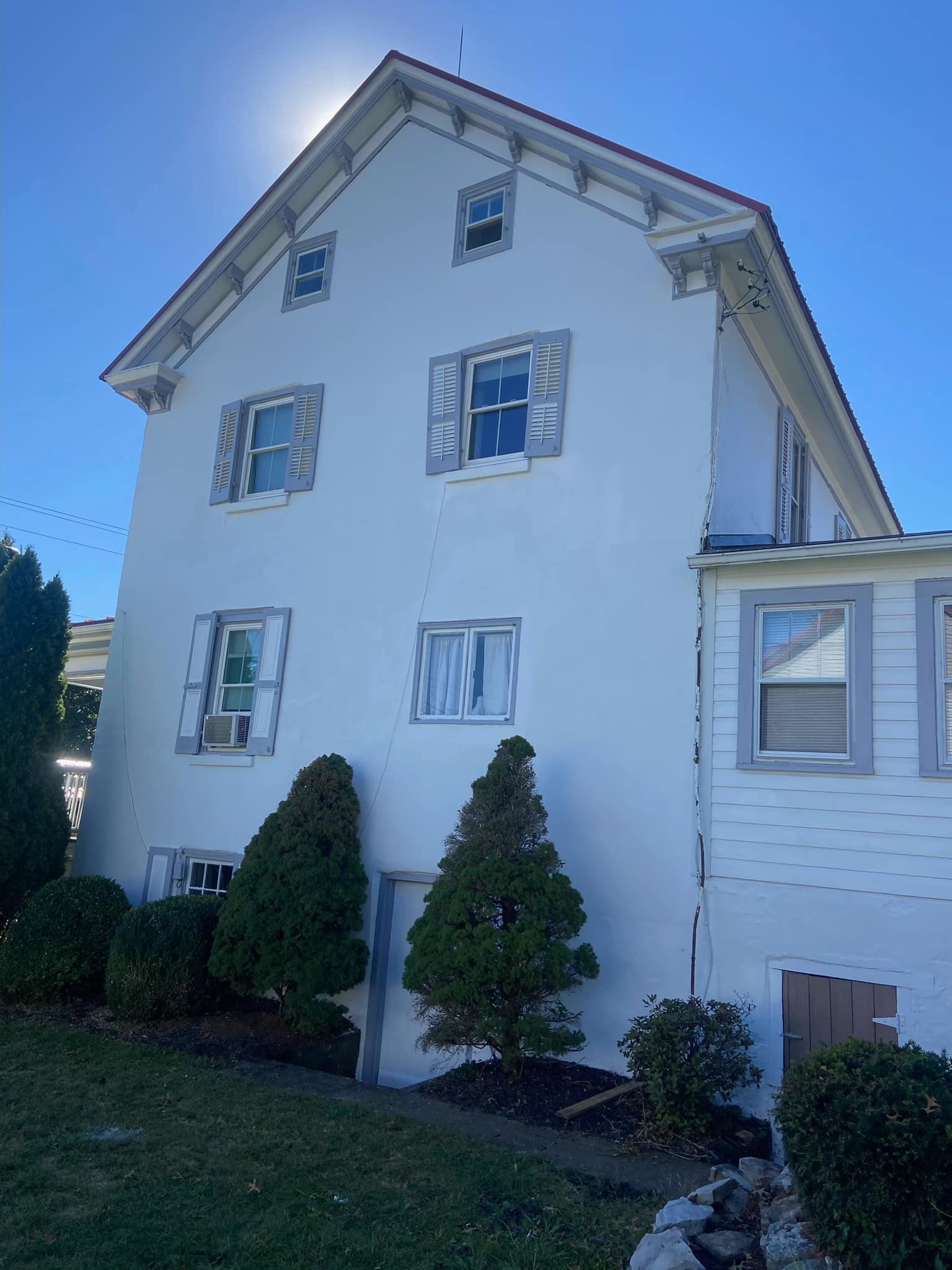 White stucco house with multiple windows, decorative trim, and blue sky.