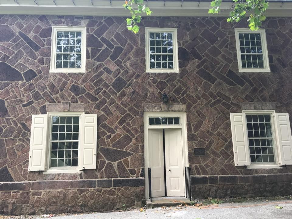 Two-story stone building with six windows and a central doorway. White shutters and trim.