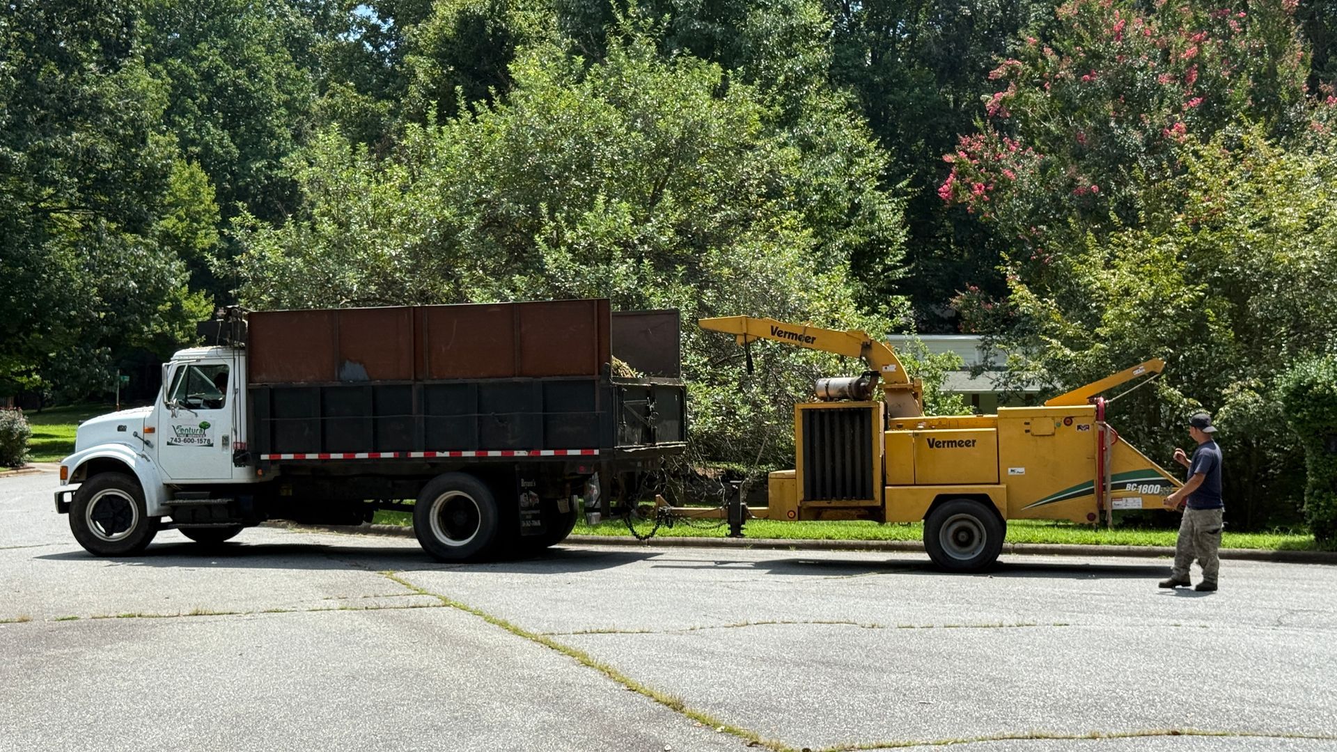 A man is standing next to a truck and a tree chipper.