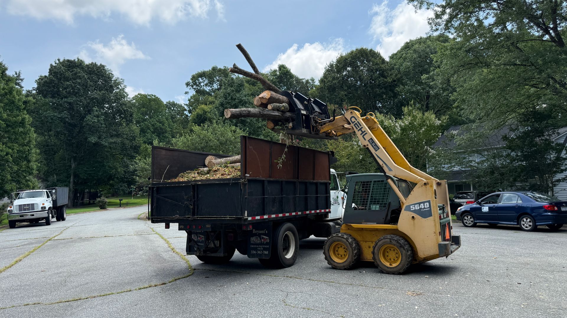 A dump truck is being towed by a forklift in a parking lot.