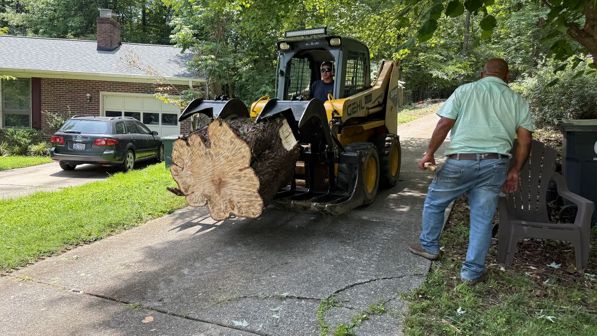 A man is standing next to a bulldozer carrying a large log.