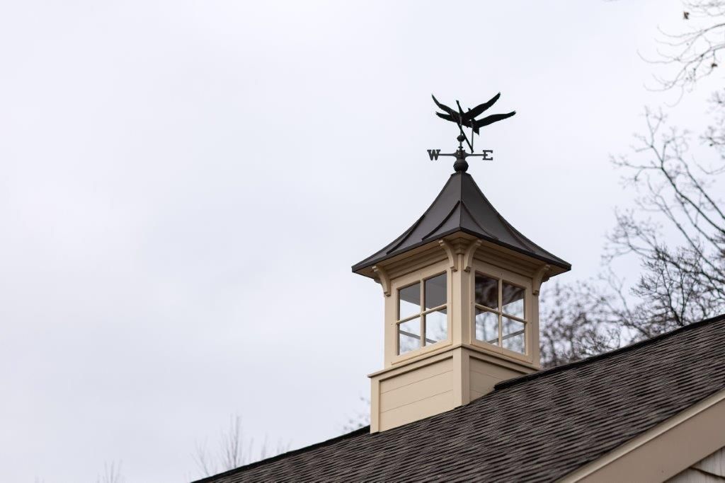Cupola with bird weathervane on a roof under a cloudy sky.