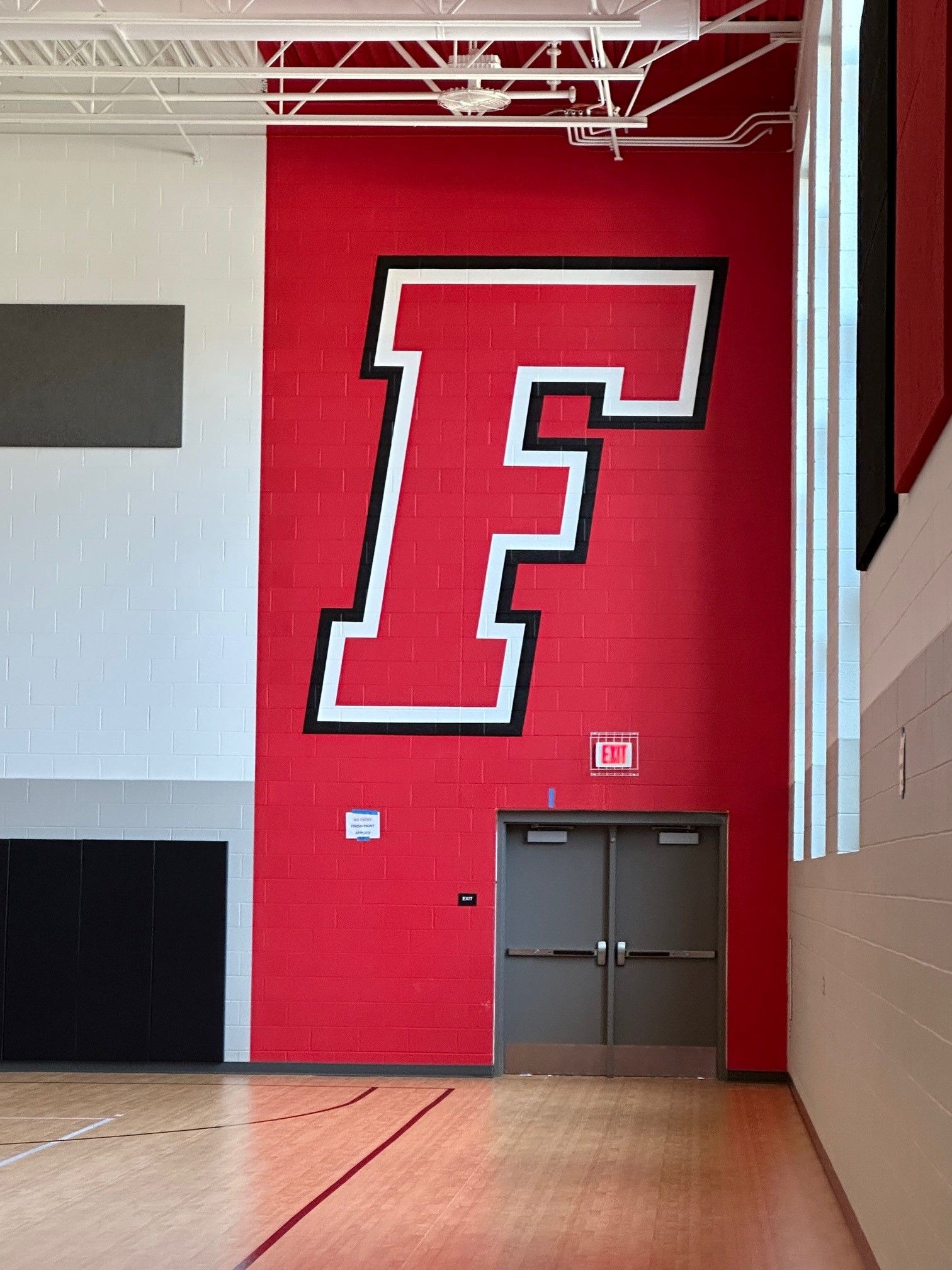 A large letter f is painted on a red wall in a gym