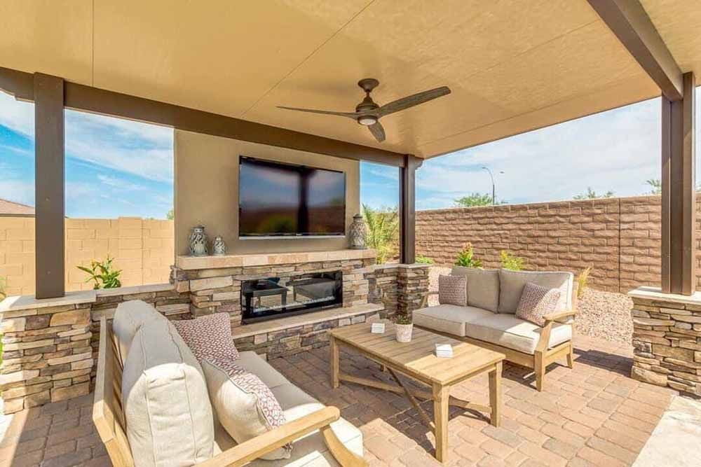 A patio with a couch , chairs , a fireplace and a flat screen tv.