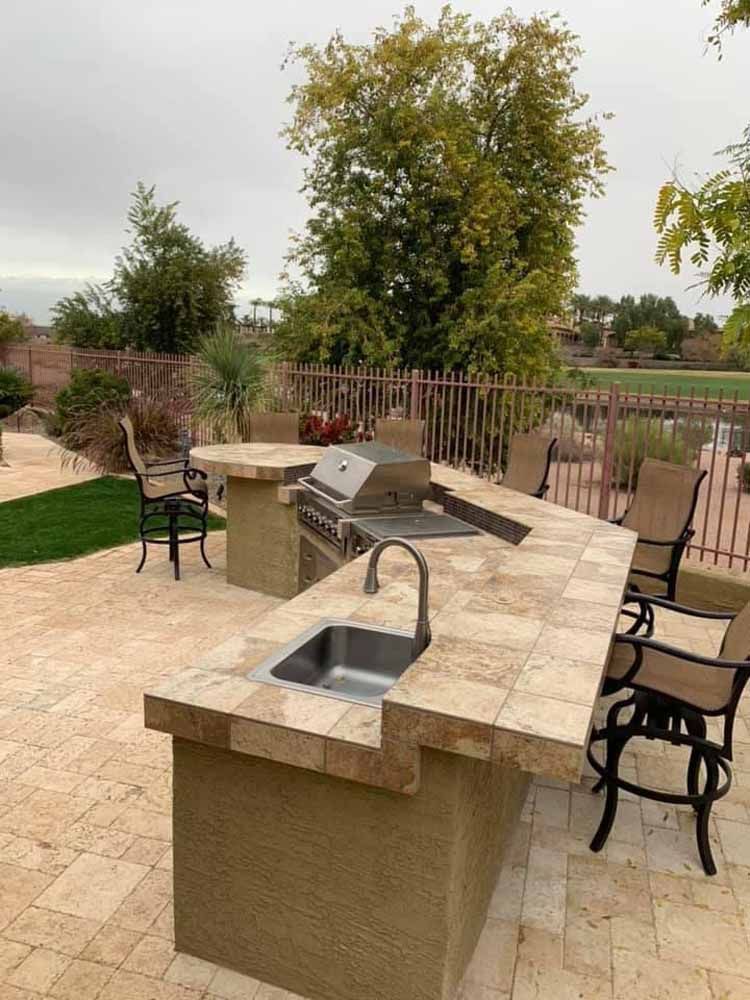 A patio with a grill , sink , table and chairs.