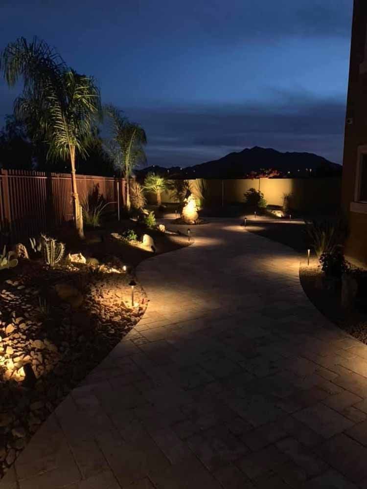 A walkway is lit up at night in a backyard.