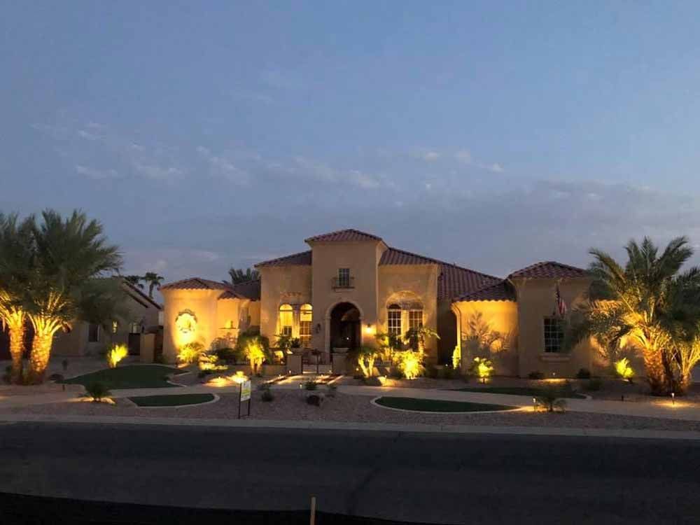A large house is lit up at night with palm trees in front of it.