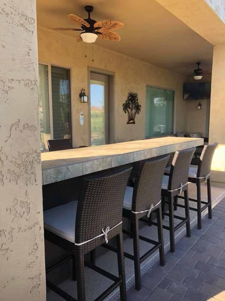 A patio with a bar and chairs and a ceiling fan.
