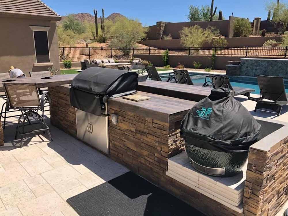 A patio with a grill , table , chairs and a pool.