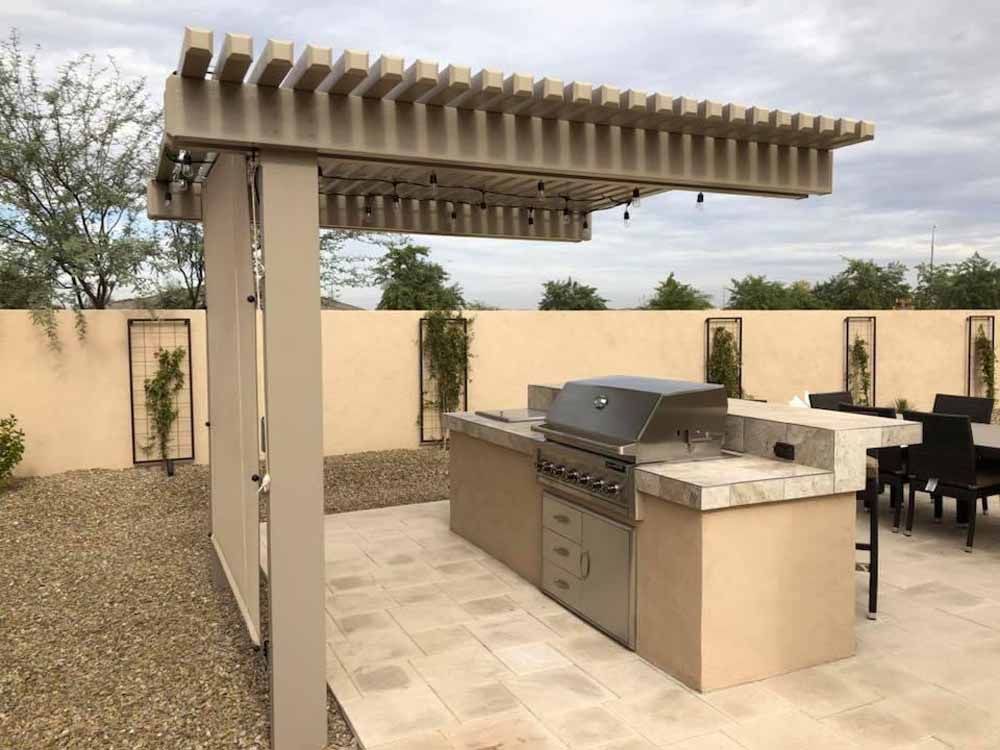 A large outdoor kitchen with a grill under a pergola.