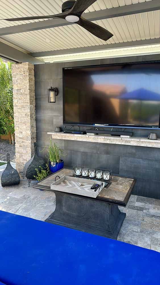 A patio with a large flat screen tv and a ceiling fan.
