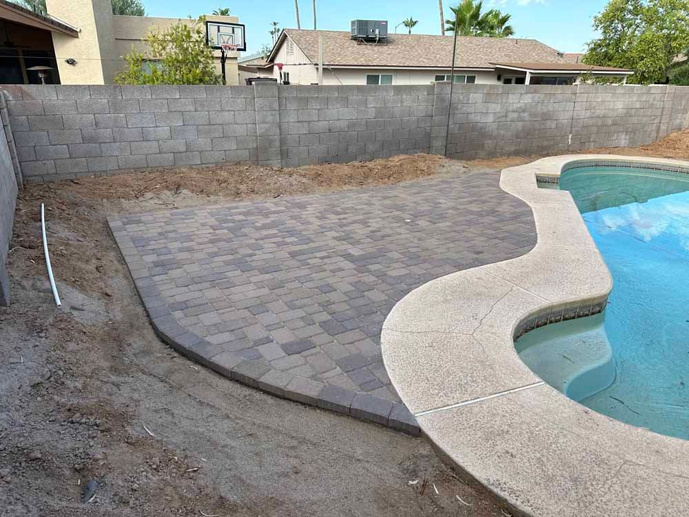 A brick wall surrounds a swimming pool in a backyard.
