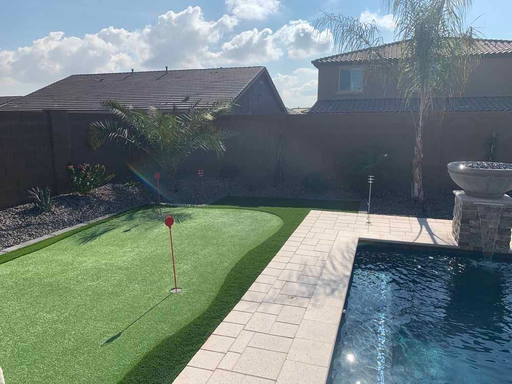 A putting green next to a swimming pool in a backyard.