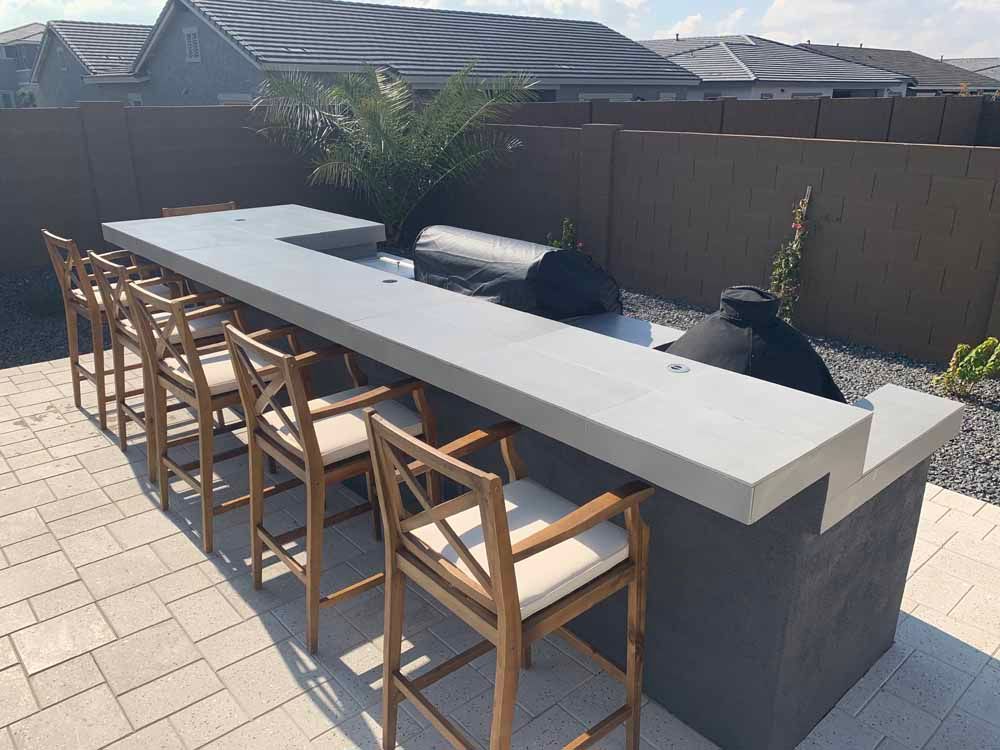 A long concrete bar with wooden chairs on a patio.