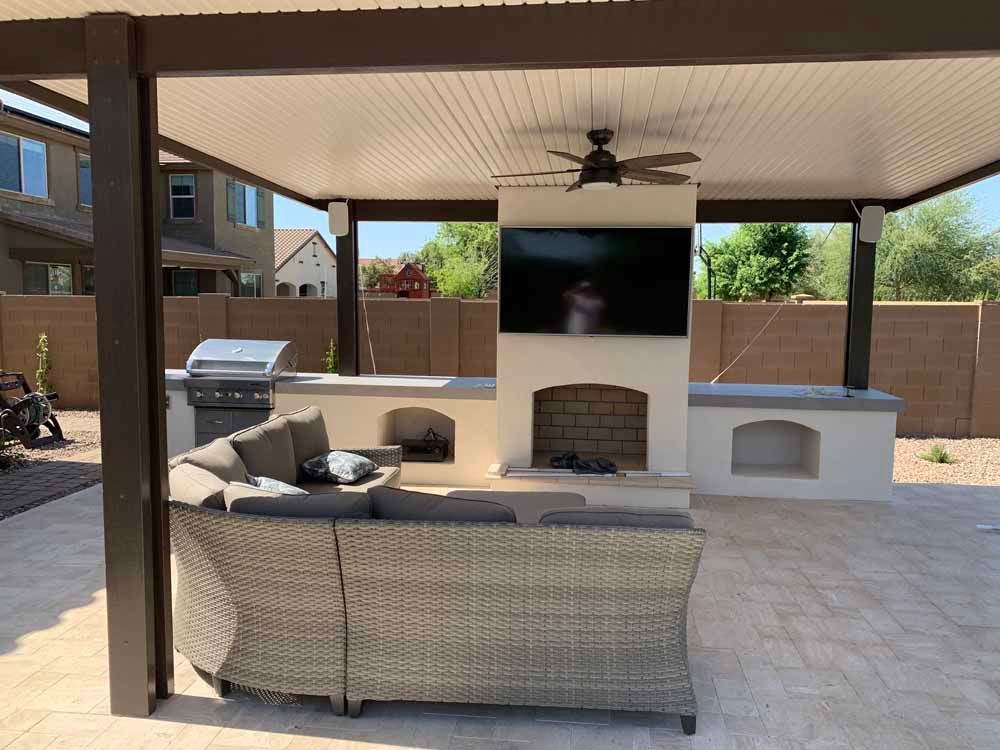 A patio with a couch , fireplace , television and grill.