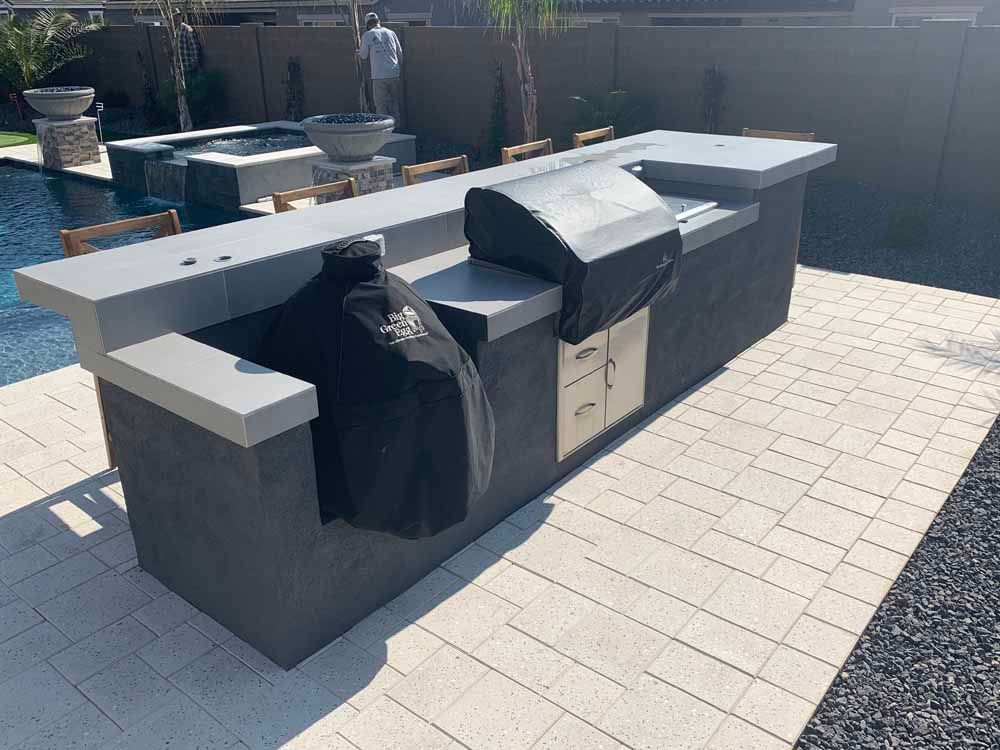 A large outdoor grill is sitting on a brick patio next to a pool.