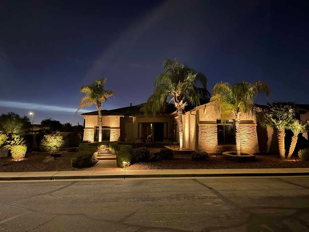 A house is lit up at night with palm trees in front of it.