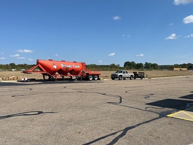A paved path winds through a bright, grassy park with scattered trees under a clear blue sky.