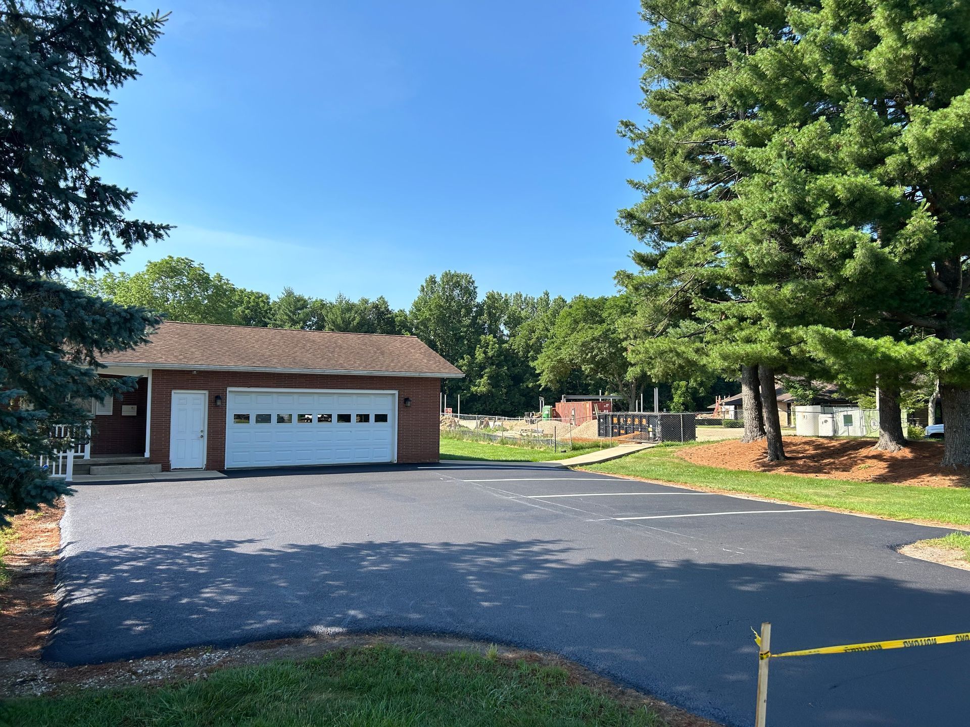Asphalt driveway in front of a small garage, trees frame the view under a clear blue sky.