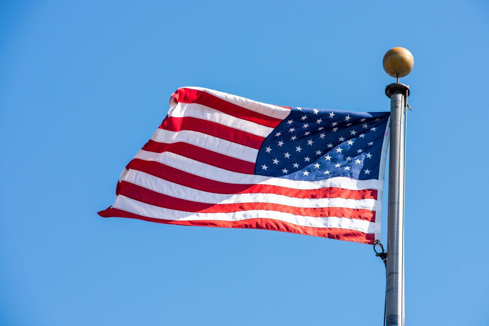 The american flag is waving in the wind on a pole.