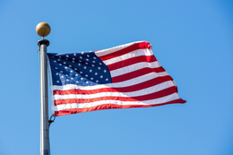 The American flag waving on a flagpole against a clear blue sky.