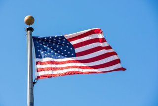 The American flag waving on a flagpole against a clear blue sky.