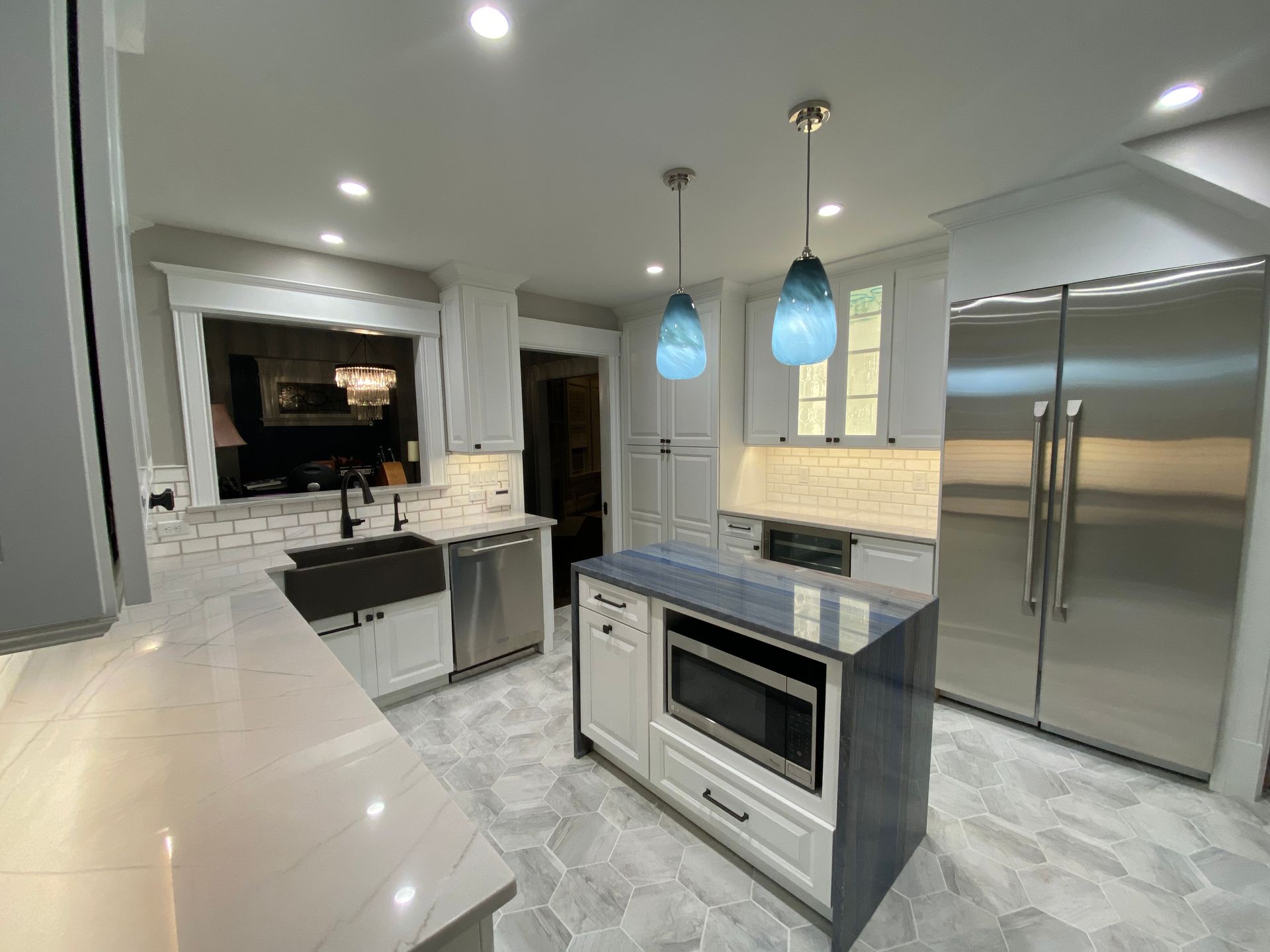 Modern kitchen with white cabinets, stainless steel appliances, and blue pendant lights.