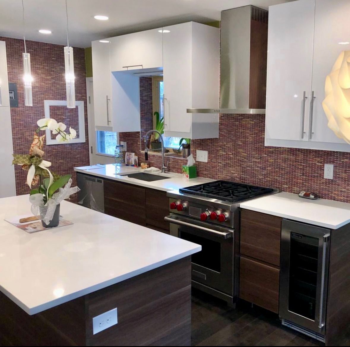 Modern kitchen with white countertops and cabinets, brown accents, and a red tile backsplash.