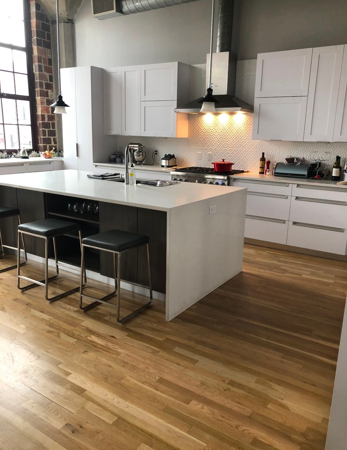 Modern white kitchen with island, wooden floor, and a large window.