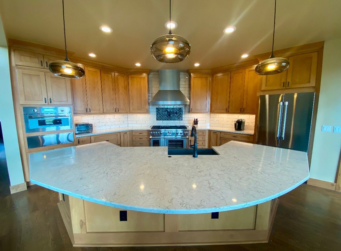 A modern kitchen with light wood cabinets, large island, stainless steel appliances, and pendant lights.