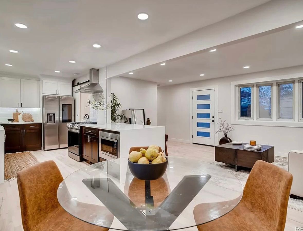 Modern kitchen and dining area with glass table, brown chairs, and white walls.