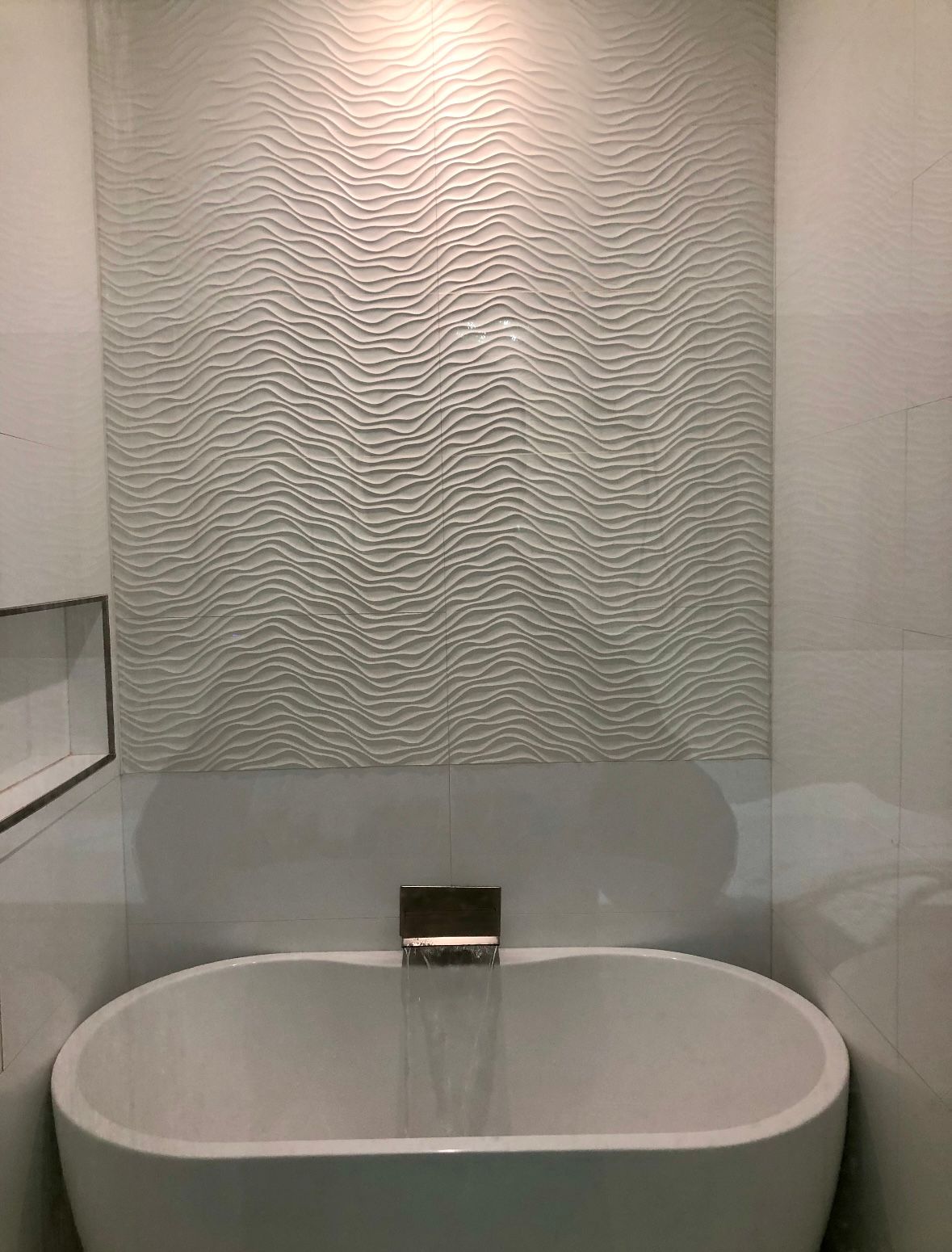 White bathtub with textured wall behind and faucet.